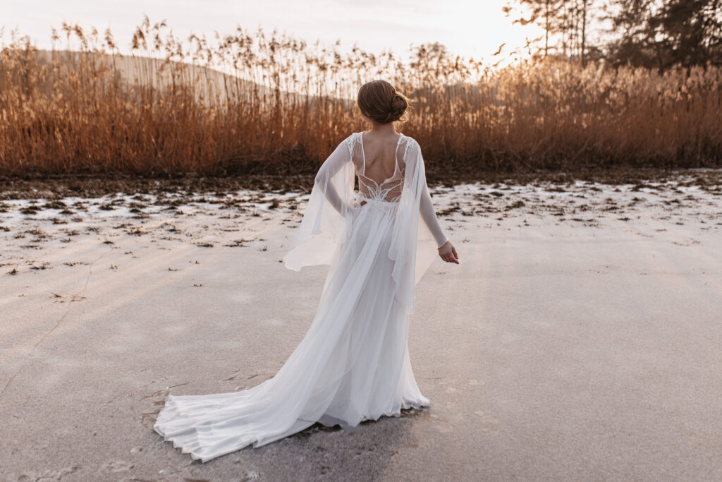 Braut im Brautkleid auf dem Eis mit Rückenausschnitt aus dem Winterhochzeitskonzept von Emma Weddings